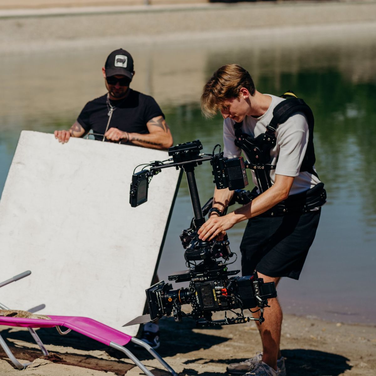 Daniel operating the Steadicam on a lake beach beside a reflector and a pink sun lounger